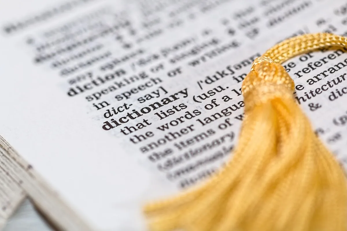 A gold tassel resting on a dictionary page, open at the entry for the word dictionary.