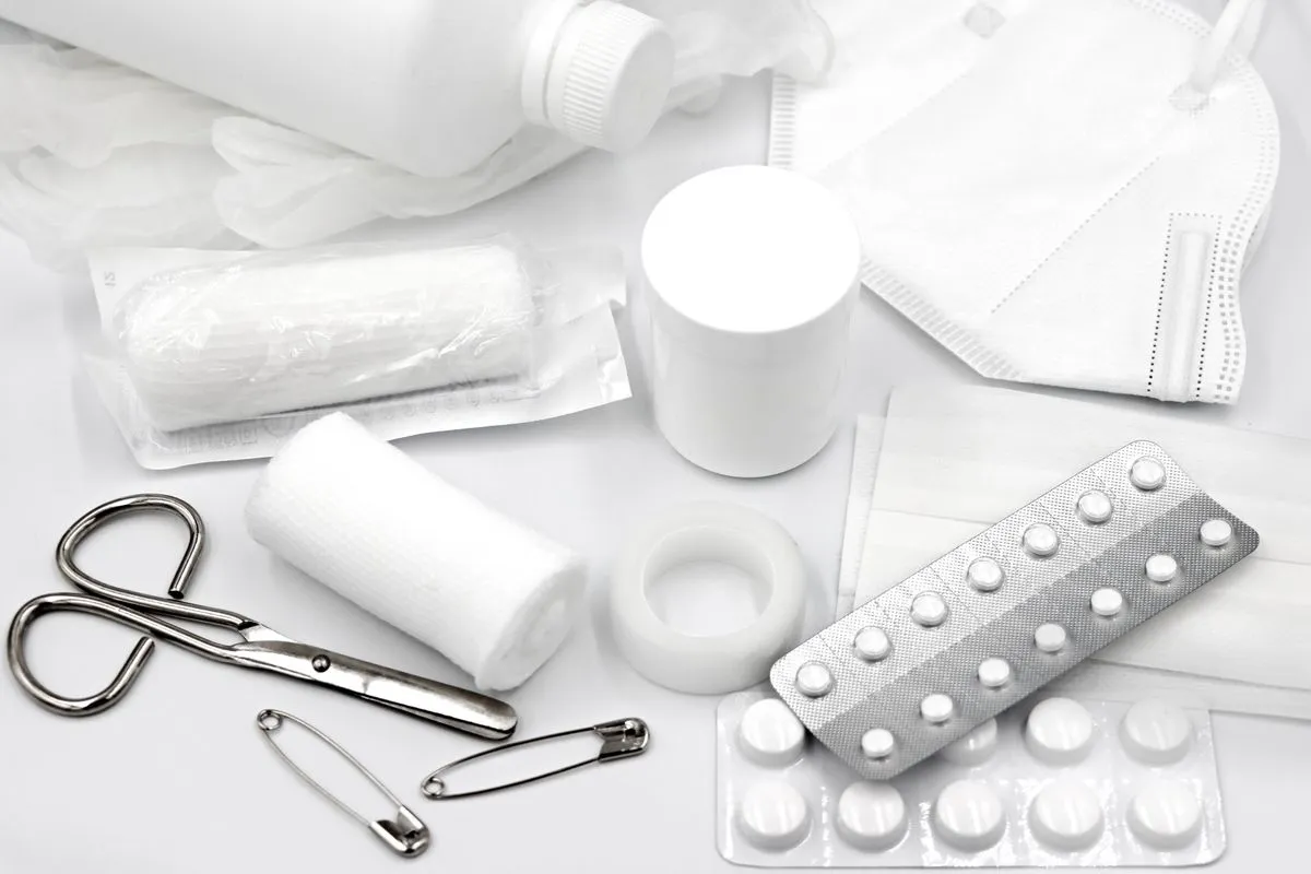 A flat lay of first aid supplies: bandages, gauze, tape, scissors, safety pins and blister packs.