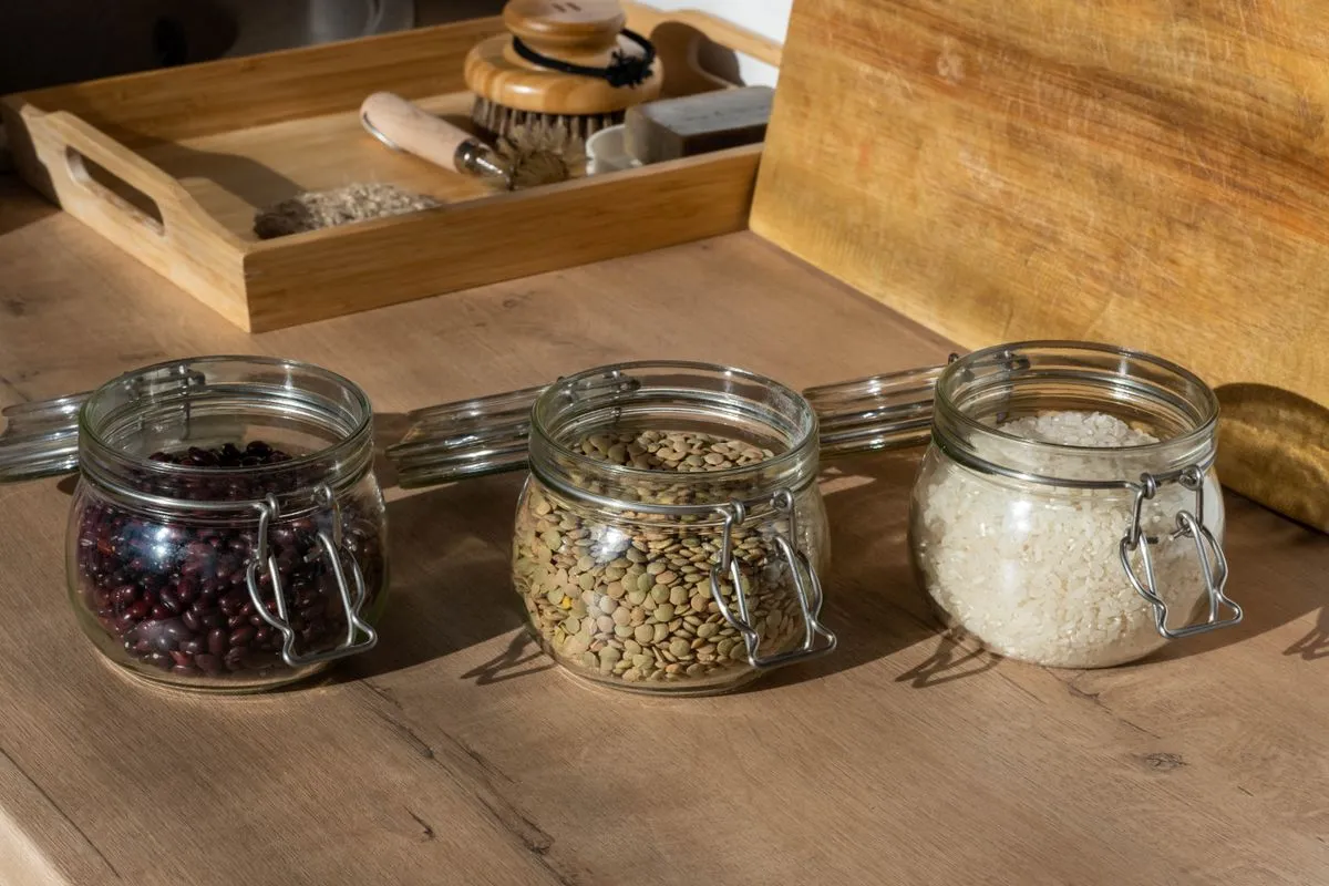 Three clip-top glass storage jars of beans, lentils and rice on a wooden worktop.