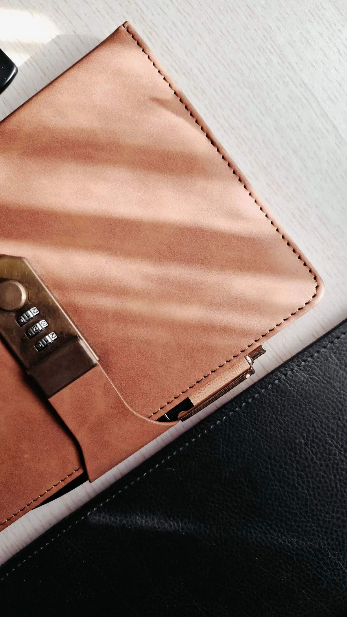 A tan leather folio with a brass combination clasp, lying on a pale desk.