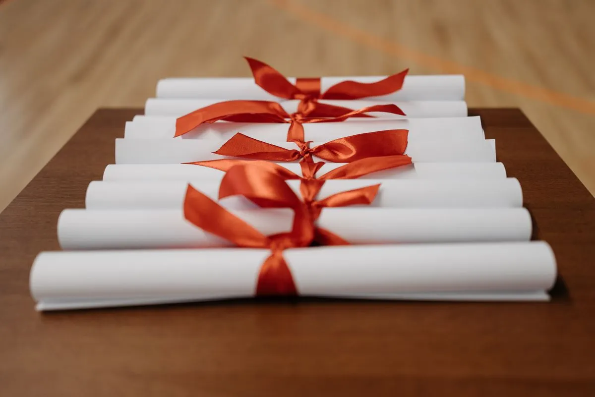 A row of rolled diplomas tied with red ribbon, laid out on a wooden table.