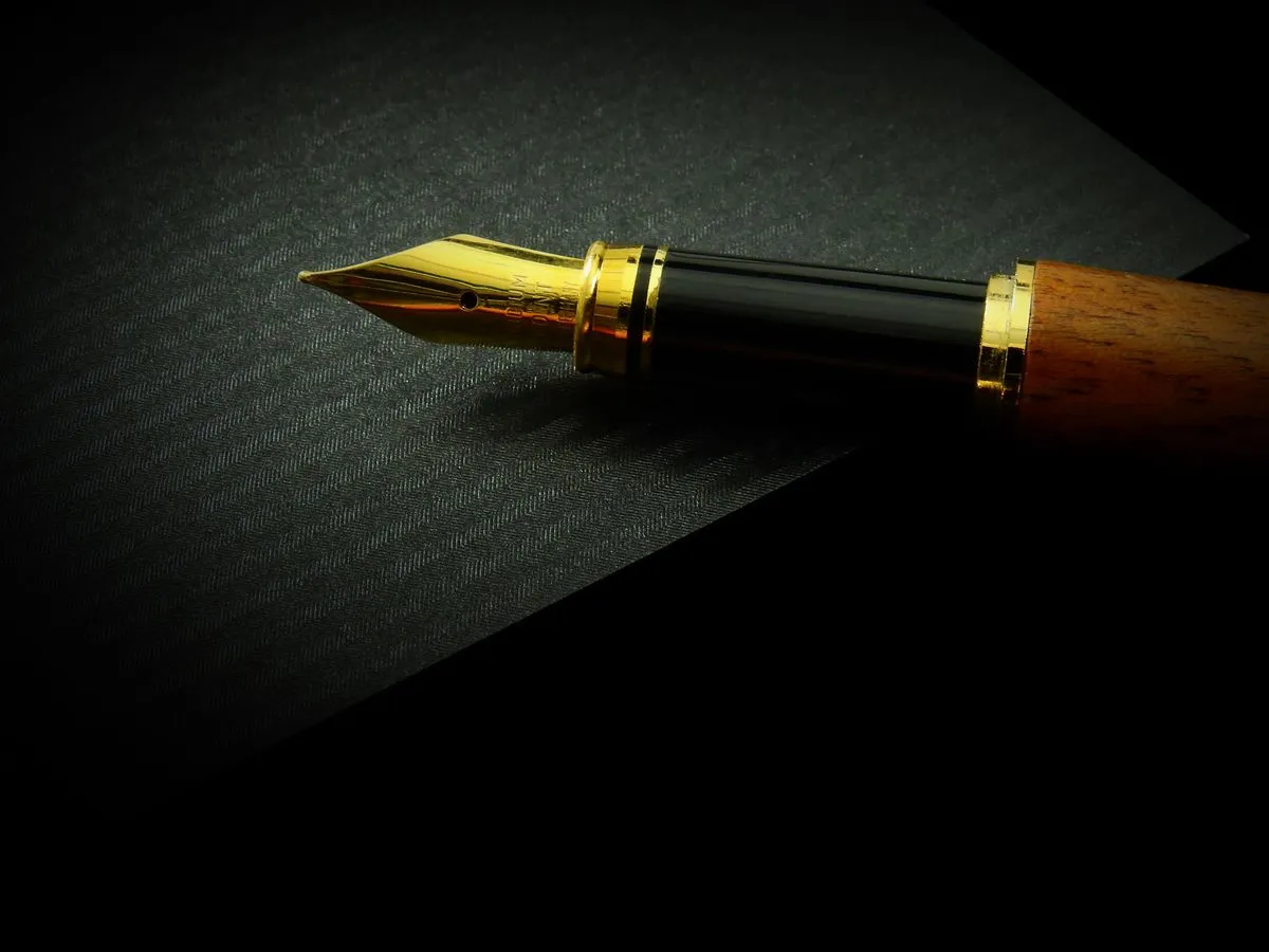 A fountain pen with a gold nib and wooden barrel resting on dark textured paper.