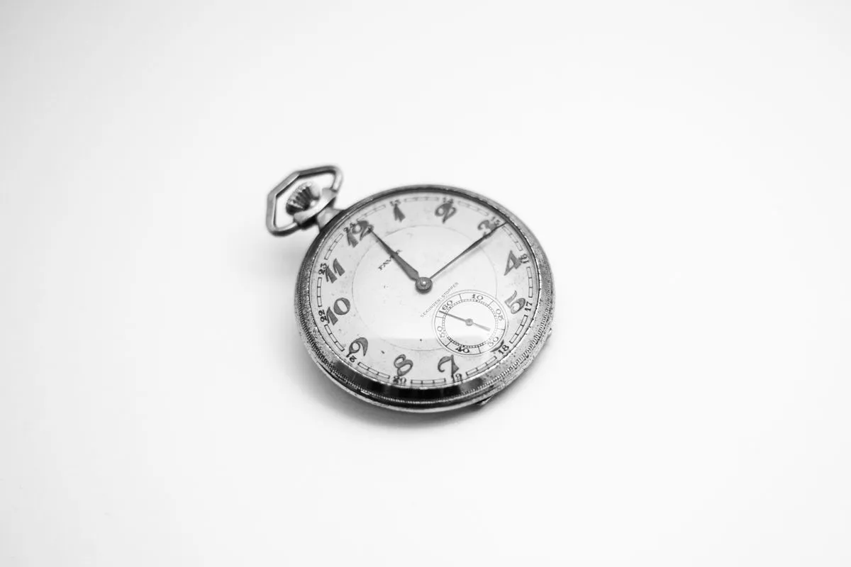 A plain silver vintage pocket watch lying open-faced on a white surface.