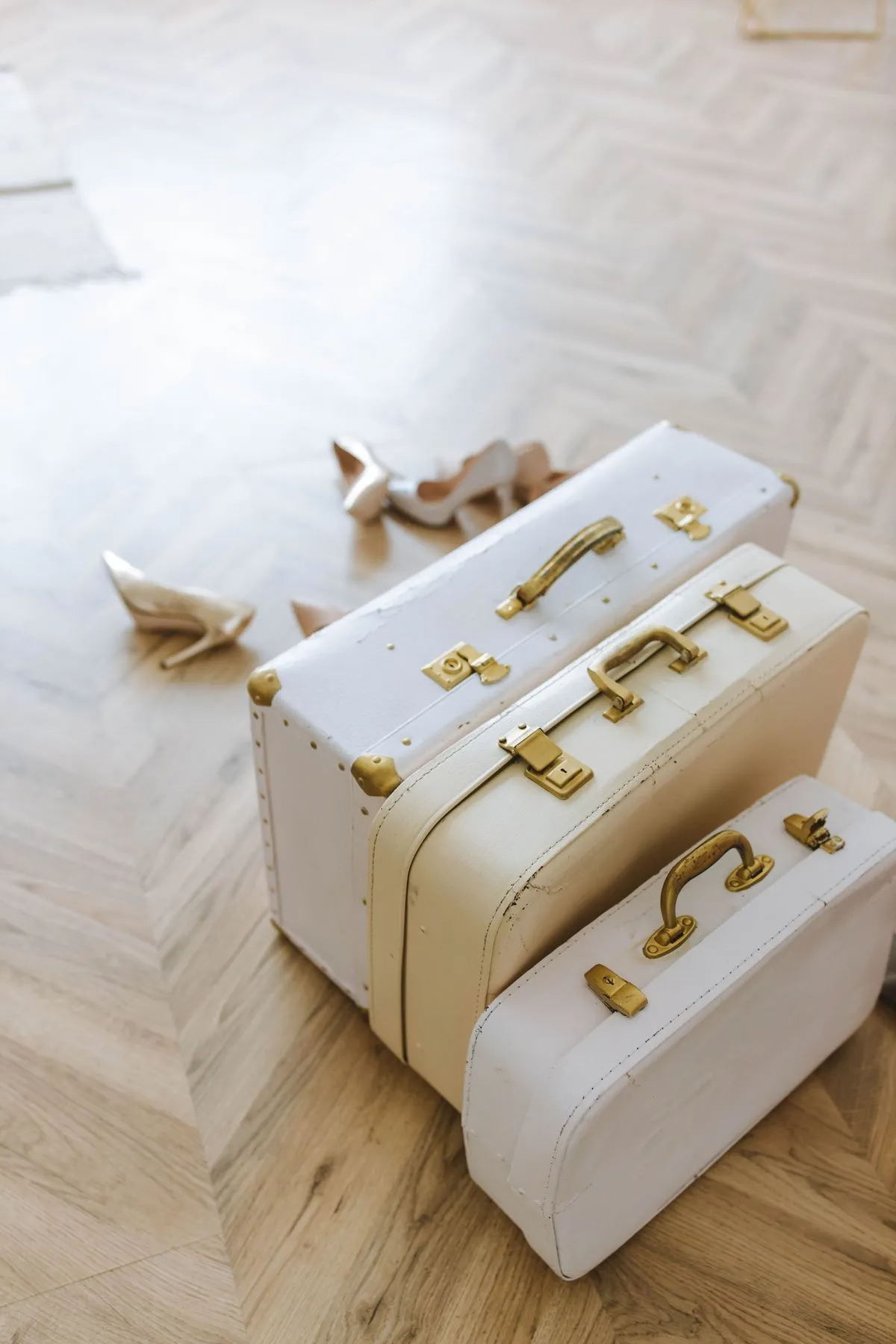 Three stacked vintage suitcases in cream and white with brass corners and catches.