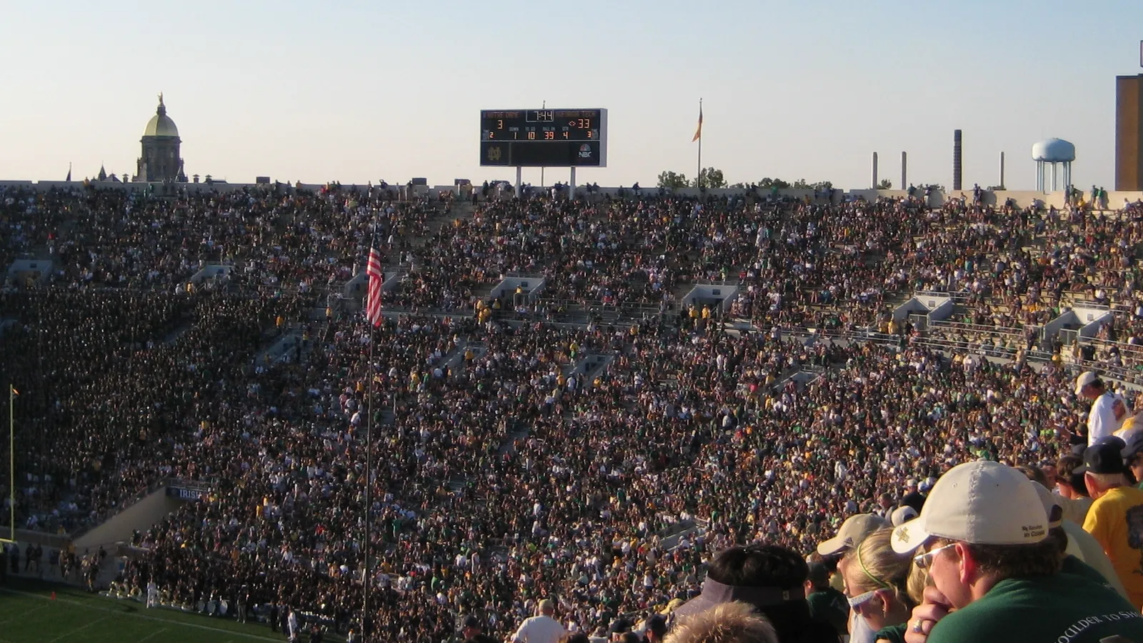 A packed Notre Dame Stadium with the Golden Dome and Touchdown Jesus mural visible in the background